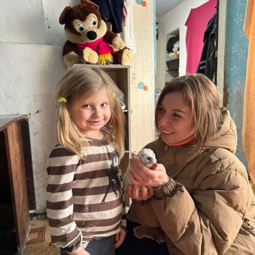 A child smiling and a person holding a new born puppy.