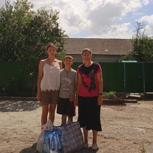 A family of three standing in front of a house.