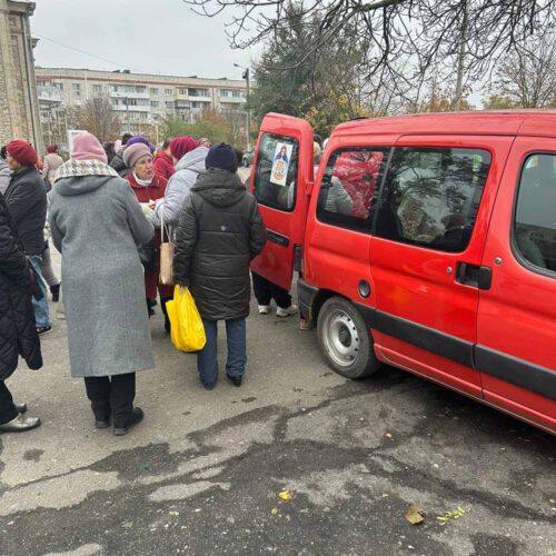 People standing near a red car and holding bags.