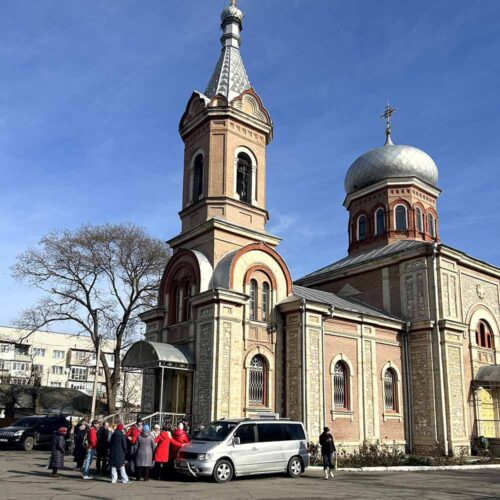 A group of people standing outside of a building next to a car.