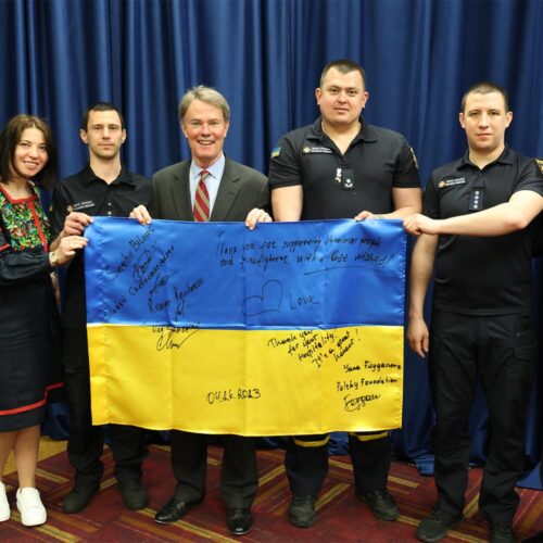 A group of firefighters and others holding a signed Ukrainian flag.