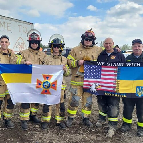 Firefighters holding up two different flags and smiling.