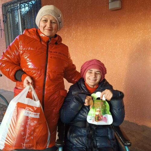 Two people smiling and holding bags of food.