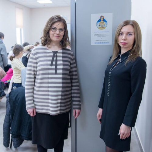 Two teachers standing by sign.