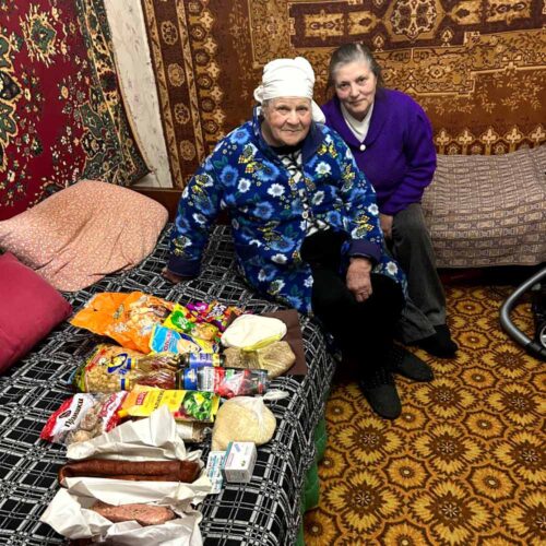 Two people sitting next to food supplies.