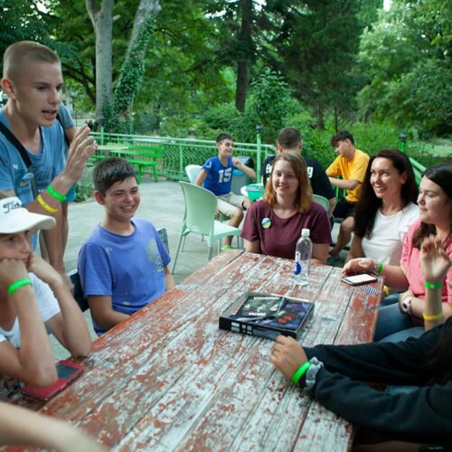 A group of children and adults sitting at a table outside together.